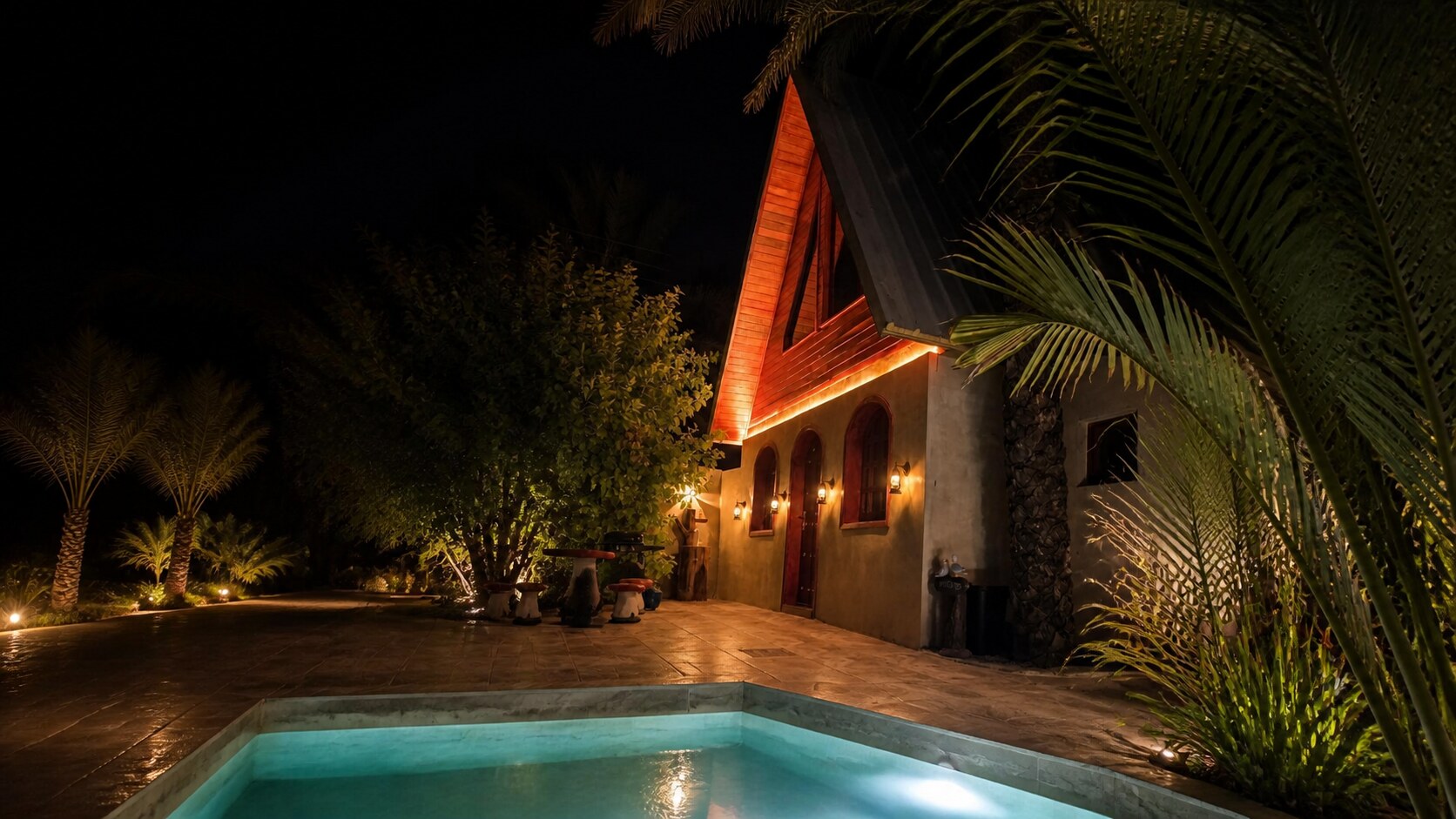 Al Asalah A-frame cottage glowing among date palms at night